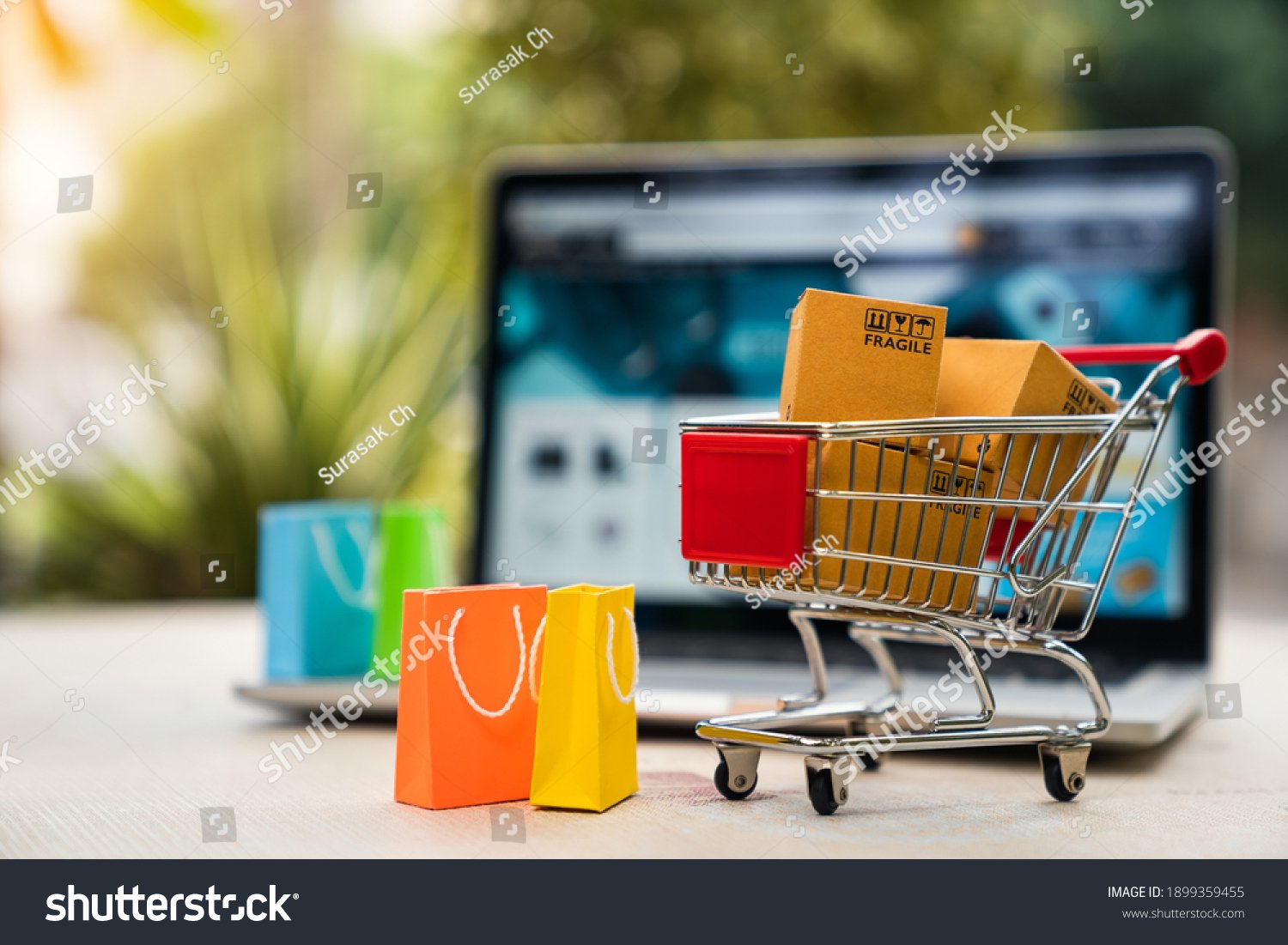 stock-photo-product-package-boxes-in-cart-with-shopping-bag-and-laptop-computer-with-blurred-web-store-shop-on-1899359455